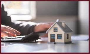 Miniature model home on a table next to a calculator 